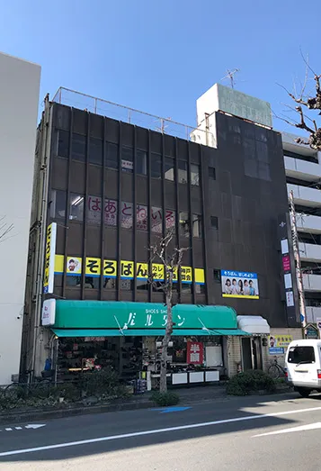 【3】ひとつ目の信号を渡り進むと、1階に緑色の屋根の靴屋さんがありますのでその建物の3階が阪急茨木店です。